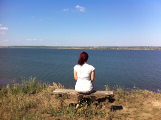 Young women sitting alone near a lake with her back turned
