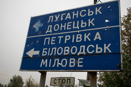 The road sign with the fragments of the projectile indicating the cities in the Ukrainian language "Lugansk, Donetsk, Petrivka, Bilovodsk, Milove" and a sign with the inscription STOP and MHC