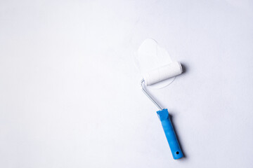 Paint roller with blue handle in white paint on white canvas, priming the canvas before painting.