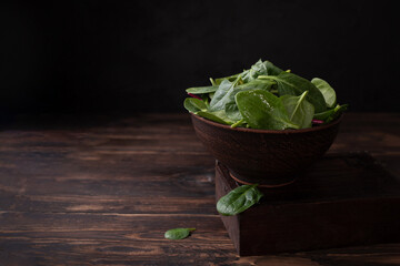 Bowl with baby spinach on a dark wooden background, healthy eating, rustic style.