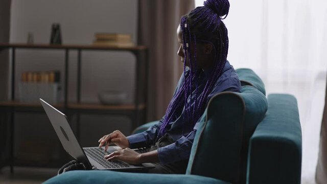 afro-american female student is learning online at home, lady is using laptop, typing text on keyboard