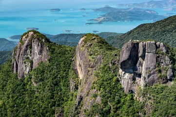 Close up view and detail of the three rock formation peaks covered with Serra do Mar green vegetation with Carioca bay coastline at far background.
