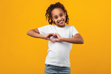 Cheerful beautiful girl making heart by hands at studio