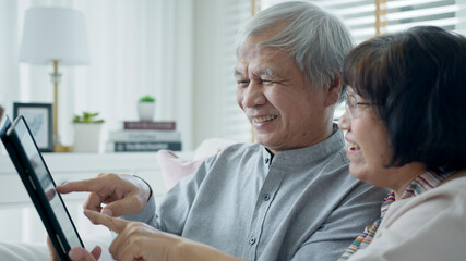 Candid old asian retired couple use tablet computer to transfer money online or financial payment and read text, smile or laugh with happy and positive. Senior asia with digital technology concept.