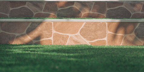 Sunlight and shadow on surface of doorsteps tile floor with blurred green artificial turf in front...