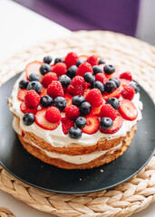 Meringue cake with fresh forest berries and cream on black plate