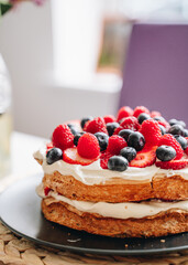 Meringue cake with fresh forest berries and cream on black plate