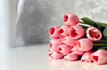 Close up image of beautiful pink tulip bouquet on white table with vase in the background in bright room.