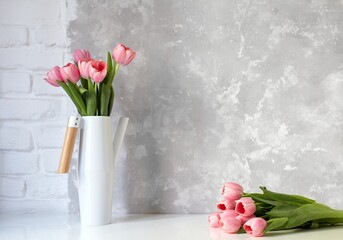 Pink tulip bouquet in vase on white table on white brick wall and bright concrete background. Copy...