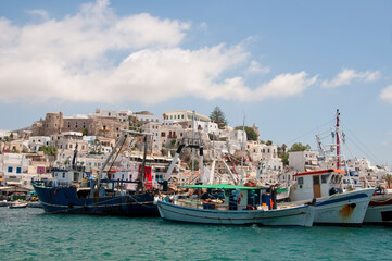 Fishing boats anchored in the old harbor of Naxos Island in Greece. In the background the castle, the city, and the partially cloudy sky.