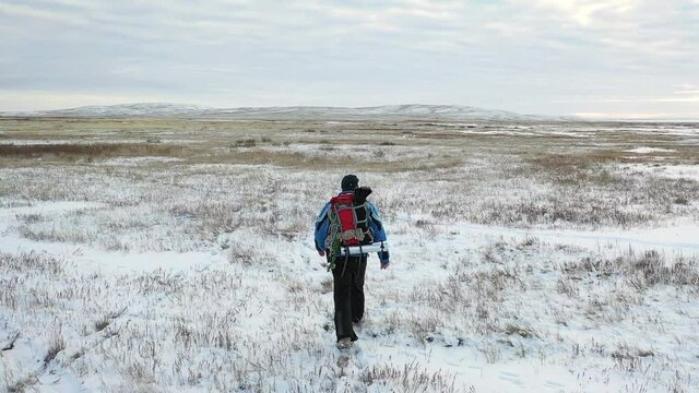 A lone hiker walks across an endless snowy field. Travel concept in extreme conditions. View from back.