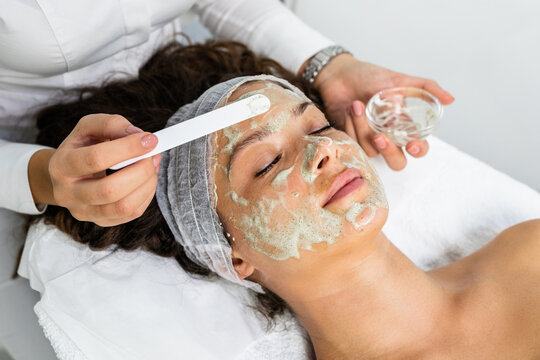 Beautiful woman receiving natural green peel facial mask with rejuvenating effects in spa beauty salon.