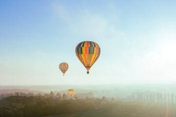 Obraz premium Bunte Heißluftballons fliegen in der frühen Morgendämmerung über eine märchenhafte Landschaft mit Bäumen