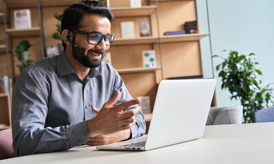 Happy indian business man remote teacher, customer support manager wearing headset talking at...