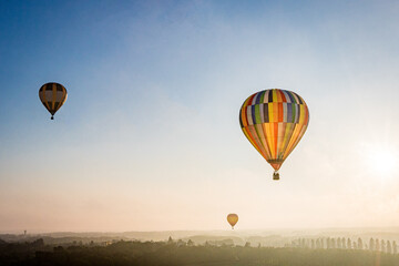 Obraz premium Bunte Heißluftballons fliegen kurz nach Sonnenaufgang über eine märchenhafte Landschaft mit Bäumen