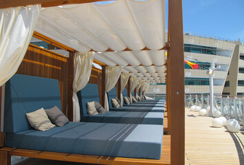 Cabana style relaxation lounge furniture deck chairs loungers under wooden pergola with white...
