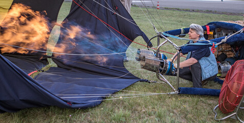 Ballonpilotin erhitzt die Luft im Inneren des noch liegenden blauen Heißluftballons mit den...