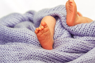 Der winzige Fuß eines neugeborenen Babys liegt auf einer blauen Wolldecke