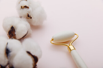 Facial massage for natural lifting. Stone roller close-up and a branch of cotton on a pink background