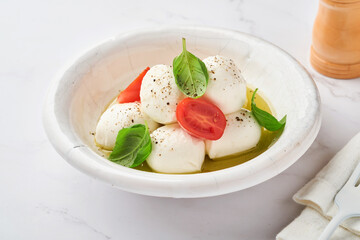 Caprese salad. Mozzarella cheese with basil and cherry tomato in white ceramic plate and tomato cherry on slate stone background, copy space. Mock up.