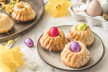 Homemade delicious mini lemon bundt cakes (muffins) and chocolate eggs on a easter table with fresh spring blossoms.