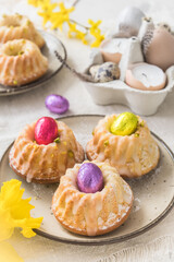 Homemade delicious mini lemon bundt cakes (muffins) and chocolate eggs on a easter table with fresh spring blossoms. Vertical.
