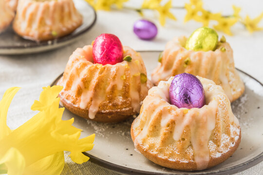 Homemade delicious mini lemon bundt cakes (muffins) with chocolate eggs on a table with spring blossoms.