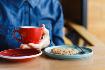 top view of a modern man in a coffee shop holding a red cup of coffee or tea and eating cookies yellow smartphone