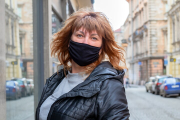 Fototapeta premium Portrait of a beautiful middle-aged woman, 50 years old, with long brown hair outdoors wearing a medical mask protecting from viruses