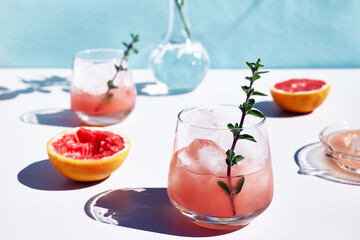 Summer grapefruit cocktail. Fresh healthy grapefruit beverage with herbs on sunlight with hard shadows. Creative drink on blue pastel background.