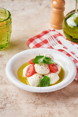 Caprese salad. Mozzarella cheese with basil and cherry tomato in white ceramic plate and tomato cherry on slate stone table background, copy space. Mock up.