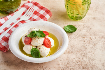 Caprese salad. Mozzarella cheese with basil and cherry tomato in white ceramic plate and tomato cherry on slate stone table background, copy space. Mock up.