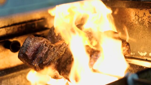 Huge flames cooking raw piece of beef rump cap on open fire barbeque