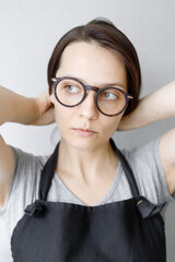 Fototapeta premium portrait of a young and beautiful Caucasian woman with dark hair and glasses, who pulls her hair back. the girl does her hair and looks thoughtfully away