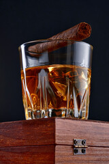 Whiskey with ice or brandy in glass with cigar on black background. Whisky with ice in glass....