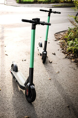 Electric scooters standing on the street in the park zone. E-scooter or kick scooter using with mobile app. Modern, ecological, eco-friendly urban transport. Summer in the city. Copy space, close up