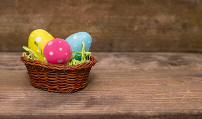 Three bright Easter eggs in a basket on a wooden background