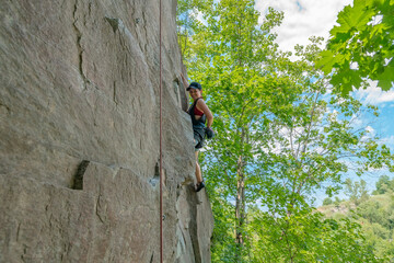 Woman climber with climbing gear equipment climbs on rock wall.