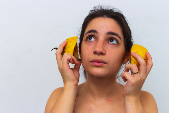 Woman with passion fruit cut in half in hands in front of her face on white background
