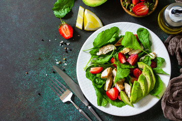 Healthy food, diet lunch menu concept, ketogenic diet and paleodiet. Summer salad with strawberries, grilled chicken and avocado on a stone table. Top view flat lay. Copy space.