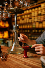 Fototapeta na wymiar Hookah maker prepares hooka for smoking in bar