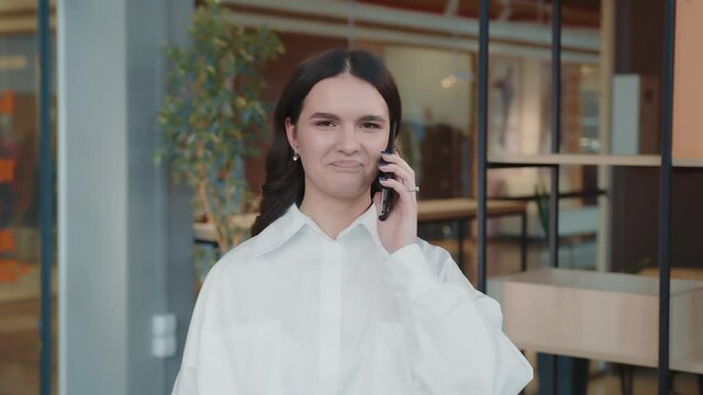 Portrait of a young girl yak in the office talking on the phone, laughing and wondering at the camera. A young student speaks on the mobile.