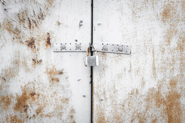 Metal door with lock texture background. White, rusty garage gate. Old worn iron plate with peeled off paint and scratches. Safety and security concept. Close up, copy space