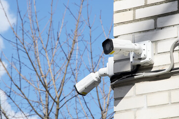 Two small white CCTV cameras on the corner of the facade of a multi-storey brick building against a blue sky