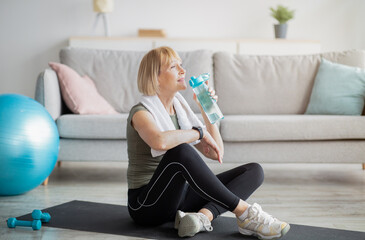 Wellness concept. Fit mature lady drinking fresh clear water from bottle after sports workout at home, copy space