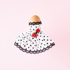 Egg wears  white dress with black polka dots.  Easter concept on a light pink background