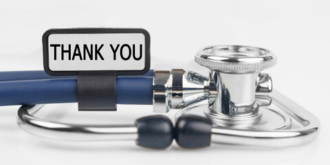 On the white surface lies a stethoscope with a plate with the inscription - THANK YOU