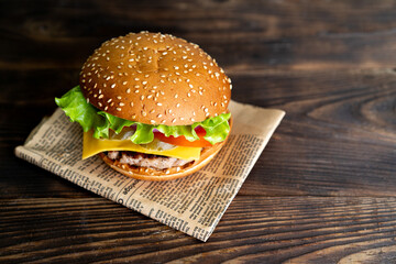 hamburger with cutlet, tomato and cheese on a dark wooden table and paper