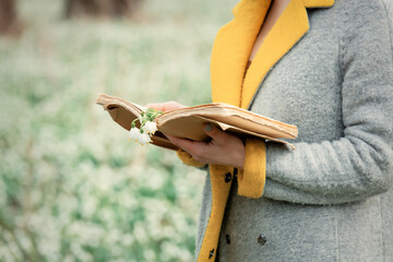 stylish girl in gray coat with a book in snowdrops meadow in forest