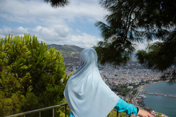 A Muslim woman at the Kyzyl Kule tower in Alanya. Sea in Turkey, Alanya through trees. Lighthouse in the background. View from above